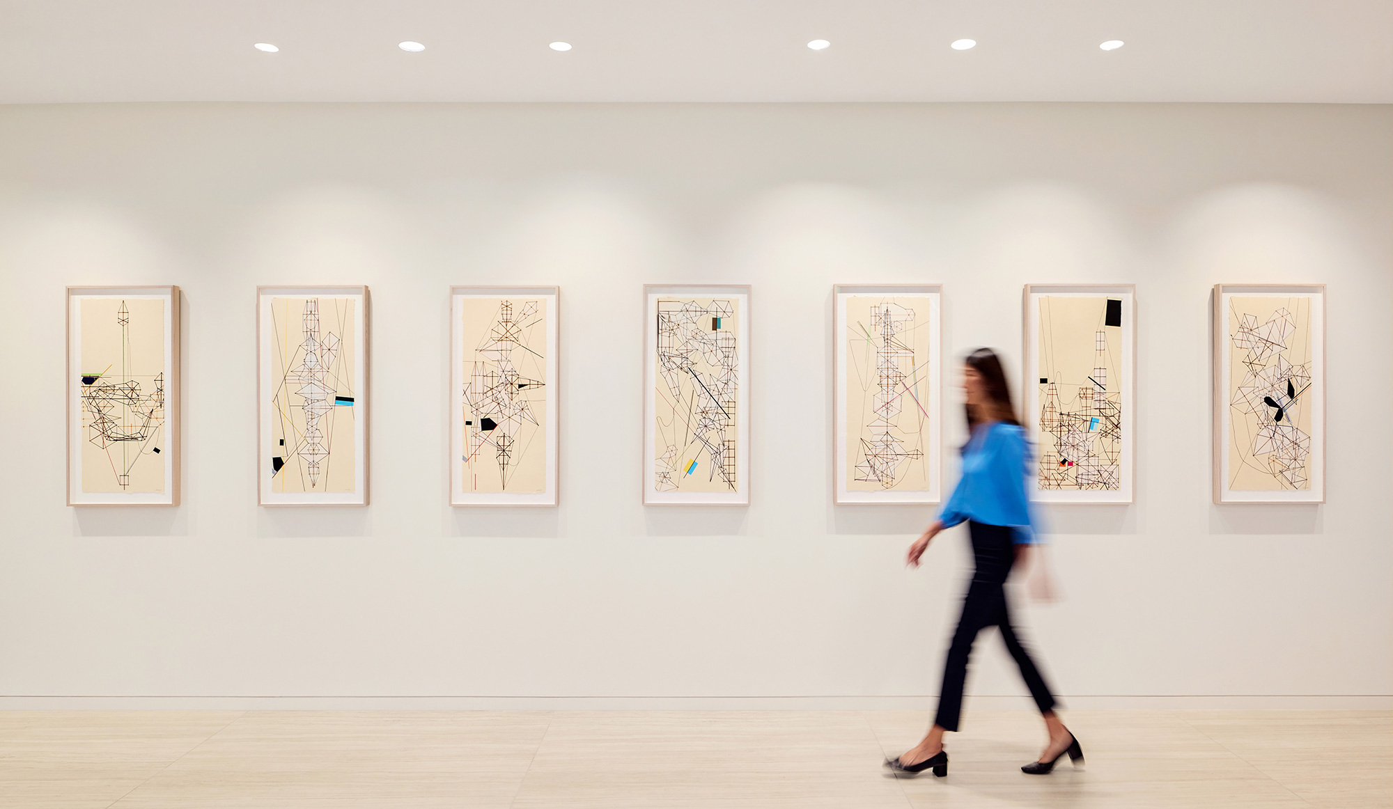 A person walking in a room with many framed pictures on the wall.