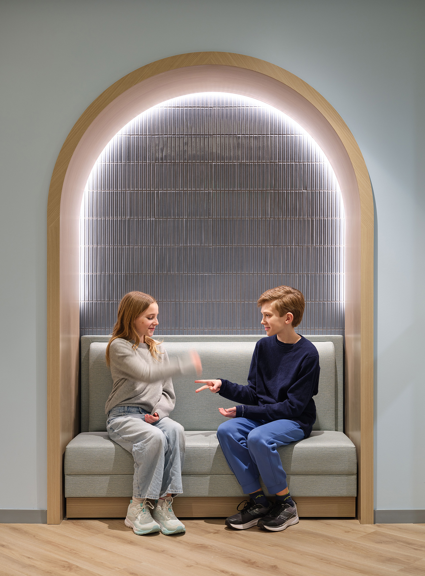 A person and a boy sitting on a bench in front of a window.
