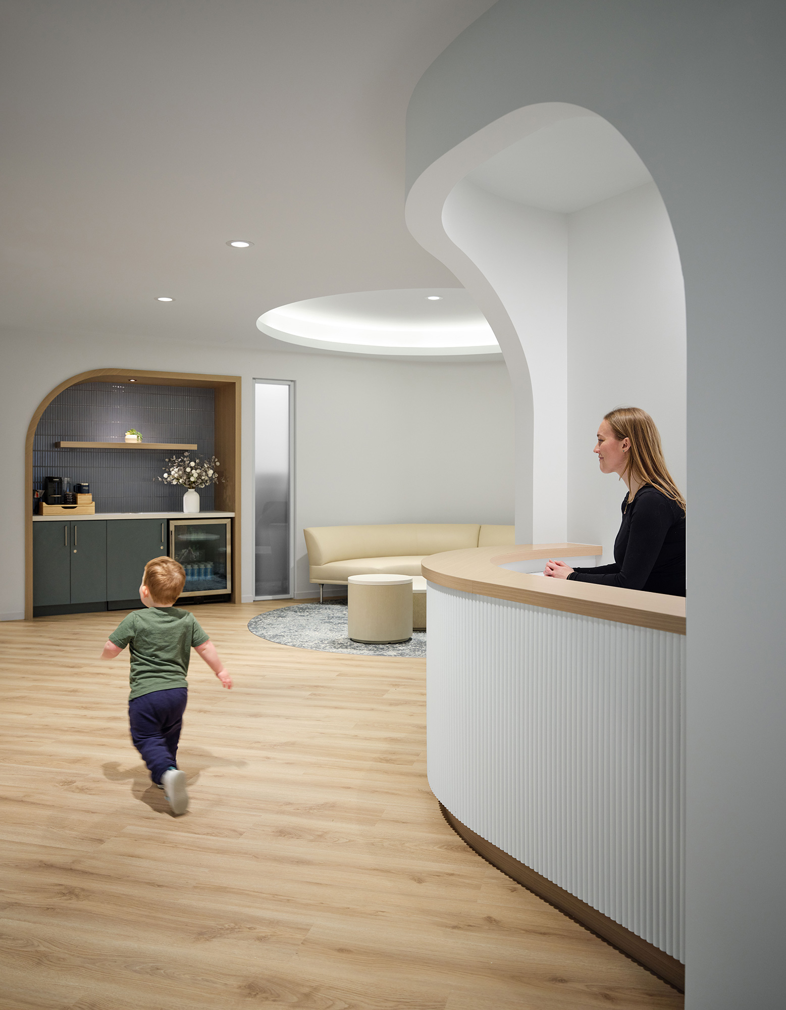 A person and a child in a room with a white table and a person sitting at a desk.