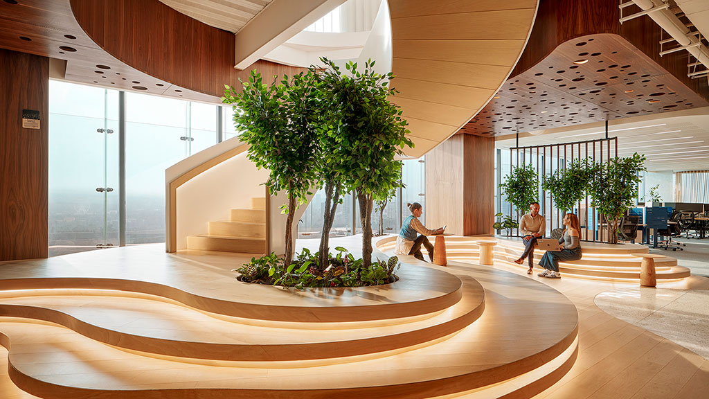 A group of people sitting on a bench in a large room with trees.