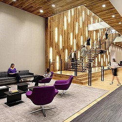 People sitting on benches in a large room with a staircase.