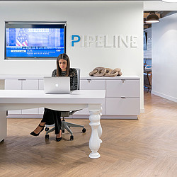 A couple of women sitting at a desk with a laptop and a tv.