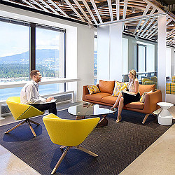 A man and woman sitting on a couch in a room with windows.