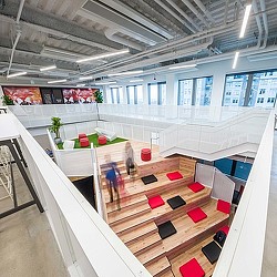 A room with a staircase and a table with chairs and a person standing at the end.