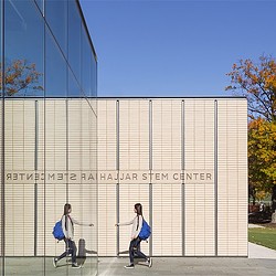 A couple of women walking by a large white building with a sign on it.