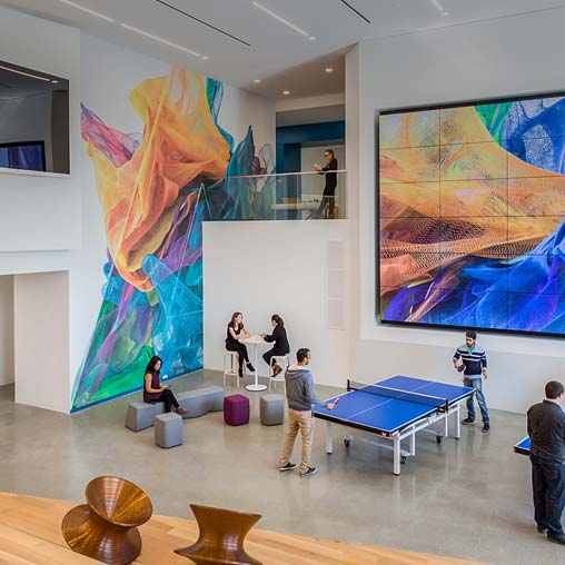 People playing ping pong in a room with large paintings.