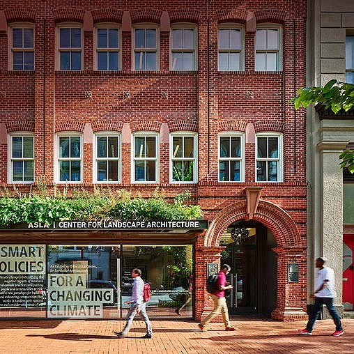 A few people walking in front of a brick building.
