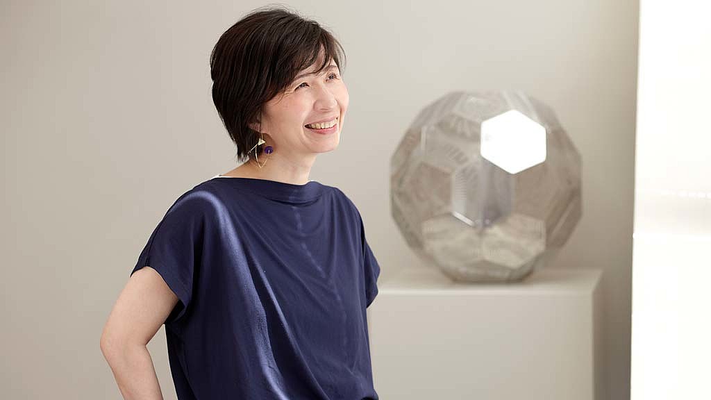 A person smiling next to a sculpture.