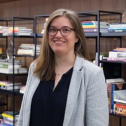 A person smiling in front of a bookshelf.