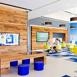 A couple of people sitting at a table in a room with a large screen and chairs.