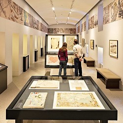 A man and a woman standing in a room with art on the walls.