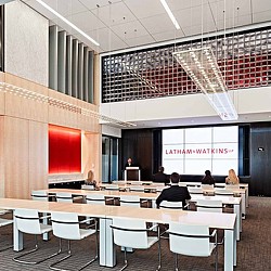 A room with tables and chairs and a screen with a group of people sitting at it.