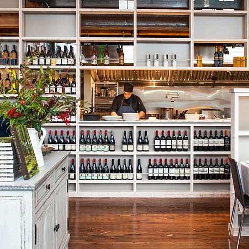 A person behind a counter with bottles of wine.