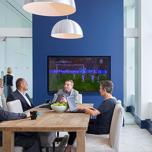 A group of men sitting at a table with a projector screen.