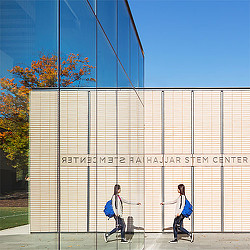 A couple of women walking by a gate with a building in the background.