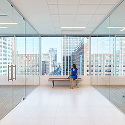 A person sitting on a bench in a large room with large windows.