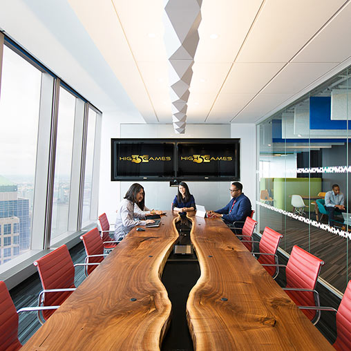 A group of people sitting at a table in a room with a large screen.