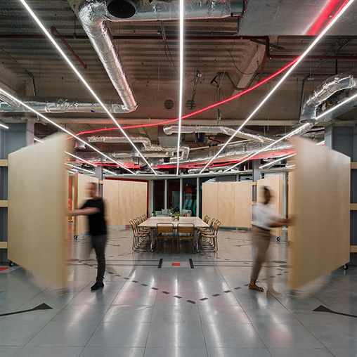 A couple of people walking in a large room with tables and chairs.