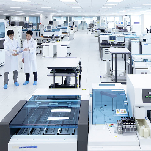 A couple of men in white coats in a room with several machines.