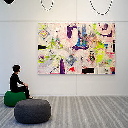 A person sitting on a chair in front of a large piece of art.