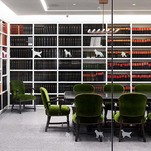 A room with green chairs and a table with books on shelves.