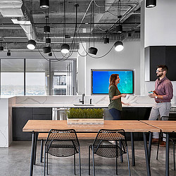 A man and a woman standing in a room with a large screen.