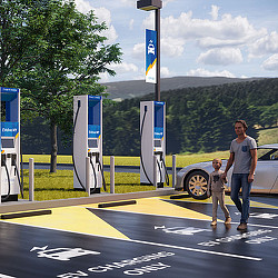 A man and a woman walking on a road next to a parking lot.
