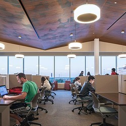 A group of people sitting at desks in a room with large windows.