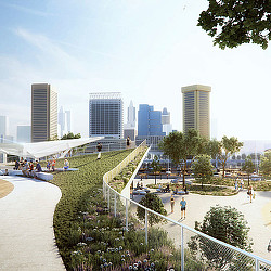A park with a fence and trees and a city in the background.