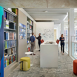 A group of people standing in a room with shelves and a white board.