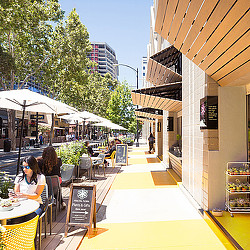A group of people sitting at tables outside of a restaurant.