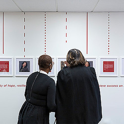 A few women looking at a framed picture on a wall.