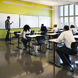 A person standing in front of a classroom with people sitting at desks.