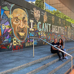 A couple of people sitting on a staircase by a wall with graffiti.
