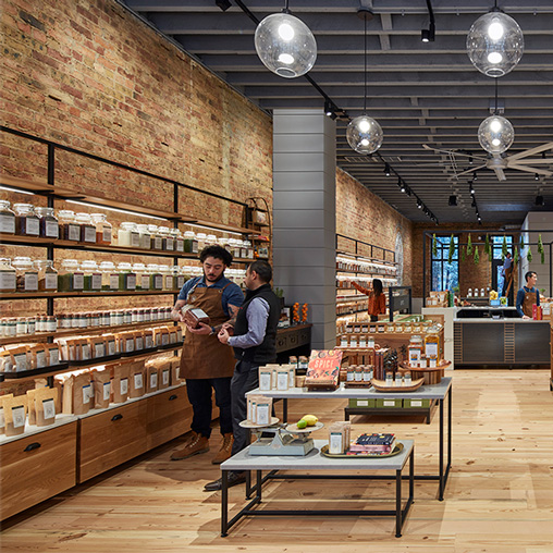 A couple of people in a room with shelves of items.