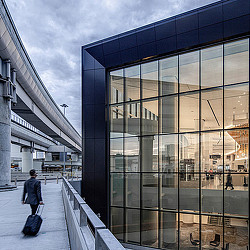 A person walking on a sidewalk next to a building with glass windows.