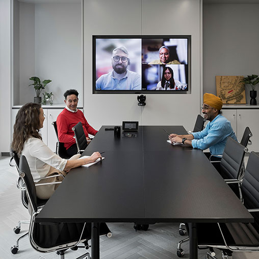 A group of people sitting around a table with a screen in the background.