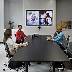 A group of people sitting around a table with a screen in the background.