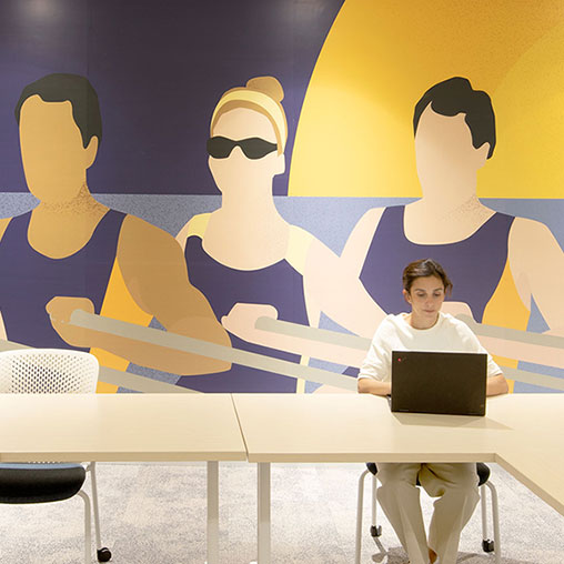 A person sitting at a table with a laptop in front of a cartoon.