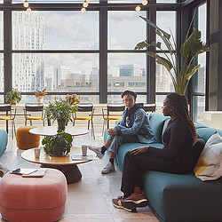 A man and woman sitting on a couch in a room with a large window.