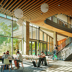 A group of people sitting at a table in a large room with windows.