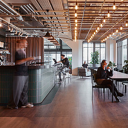 A person standing in a room with people sitting at tables and chairs.