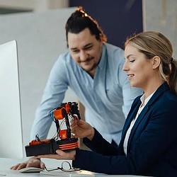 2 coworkers looking at robotic prototype at work. Credit: Getty