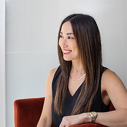 Lori Mukoyama in Gensler Chicago sitting in a red chair in front of a grey background