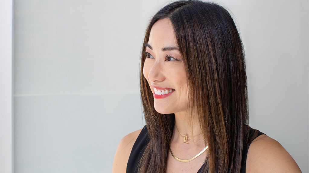 Lori Mukoyama in Gensler Chicago sitting in a red chair in front of a grey background