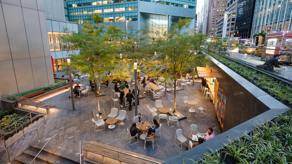 A group of people sitting at tables in a courtyard.