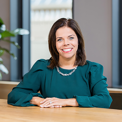 Deanne Erpelding sitting at a wooden table with a plant and windows in the background