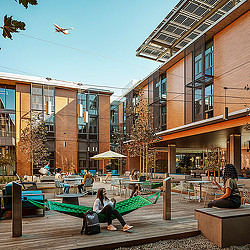 A person sitting on a bench in a courtyard with a plane flying over the.