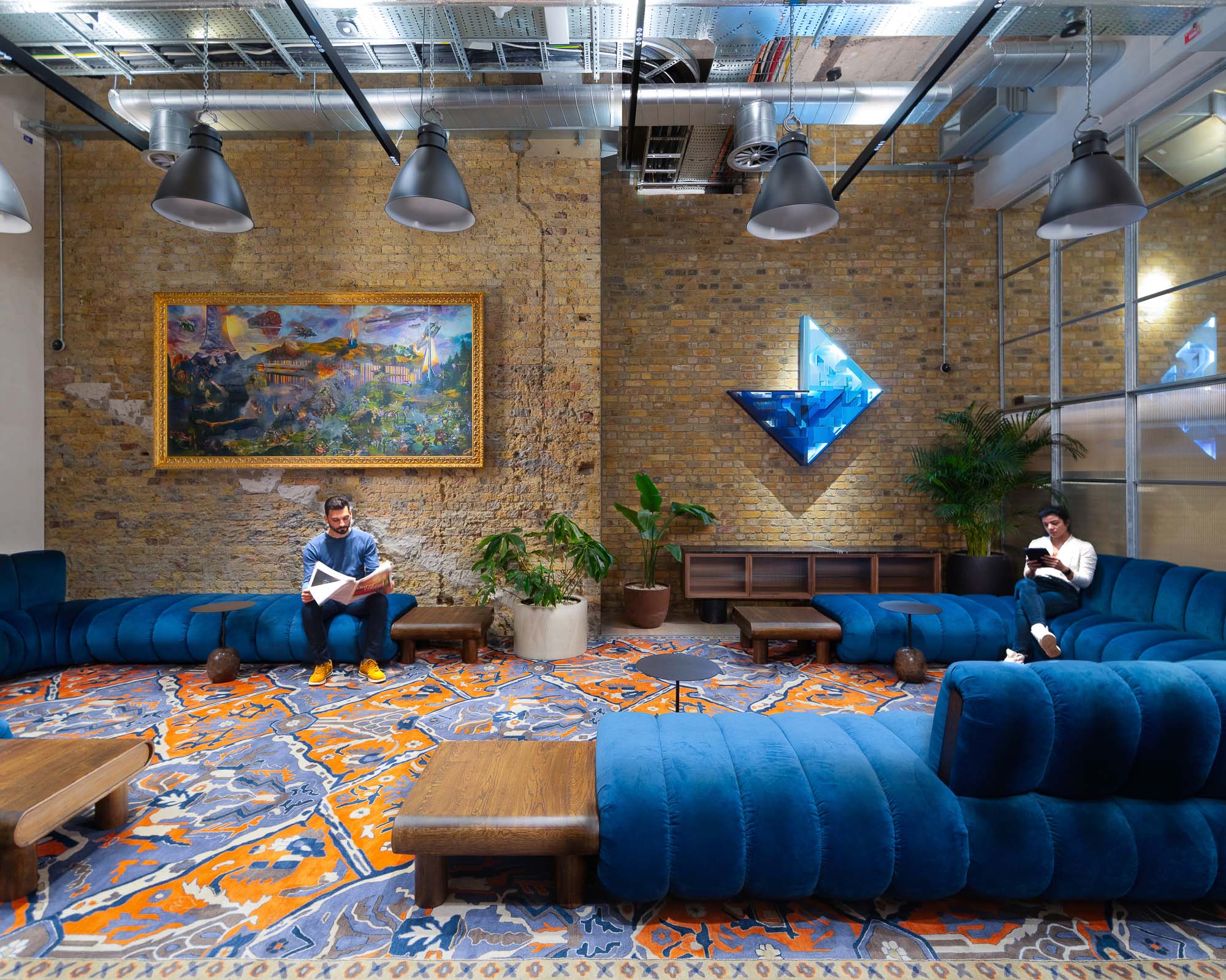 A couple of men sitting on a couch in a room with a large mural on the wall.