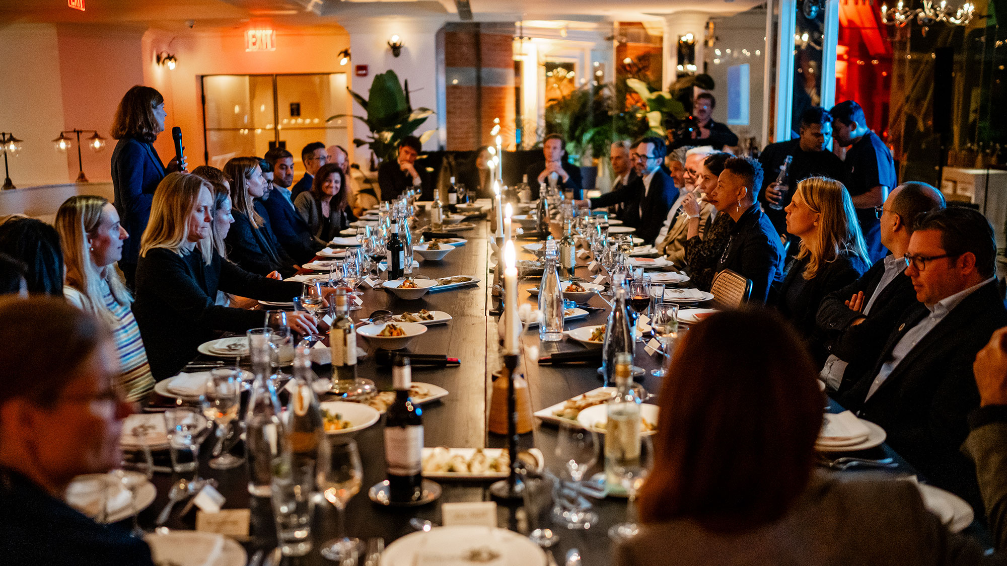 A large group of people sitting at a long table with food and drinks.